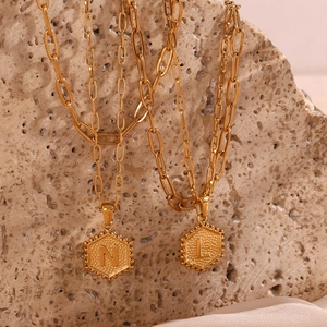 Close-up of golden hexagonal pendants with N and L initials on paperclip chains