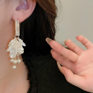 Close-up of long zircon shell earrings with white petals and pearls on a model