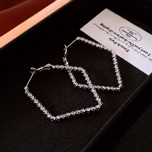 Close-up of silver geometric rhombus earrings with pleated texture on black jewelry box