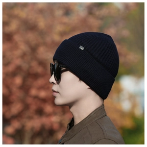 Close-up of thick navy blue knit beanie with metal brand logo and rib-stitch texture