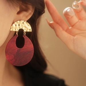 Detail of red resin drop earrings with gold textured metal worn by a model