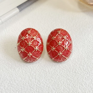 Macro shot of oval red enamel earrings with golden vintage floral patterns