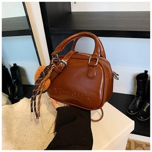 Detail of caramel brown mini handbag featuring embossed logo and a striped tassel charm