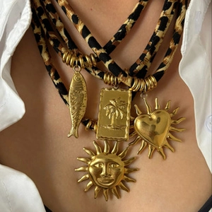 Close-up of layered gold heart and palm tree pendants with leopard print fabric cords