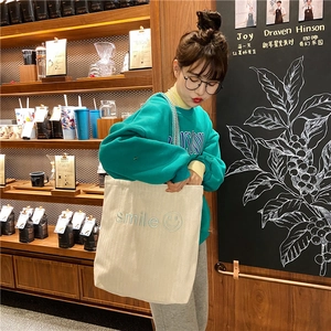 Detail of beige canvas tote bag with cyan smile embroidery and pearl shoulder strap