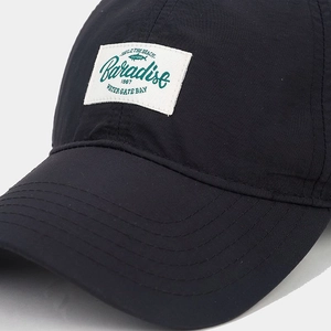 Detail of black quick-dry baseball cap featuring a white Paradise 1967 patch embroidery