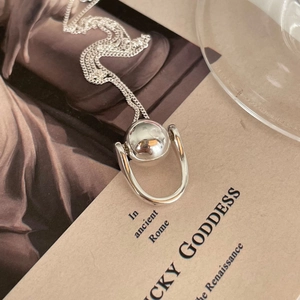 Artistic detail of a silver geometric sphere pendant necklace on vintage paper