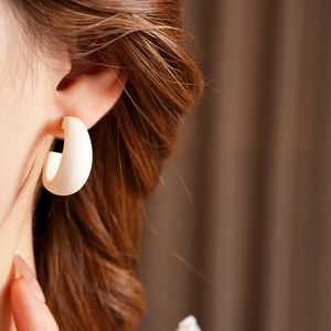 Close-up of minimalist cream-colored C-shaped wooden hoop earrings worn by a model