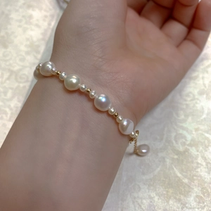 Close-up of baroque pearl bracelet with gold beads on woman's wrist and vintage fabric