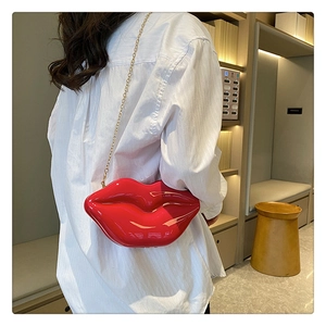 Detail of red lip-shaped crossbody bag featuring glossy finish and gold metal chain strap
