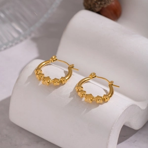 Close-up of elegant star-patterned 18K gold earrings on a textured aesthetic tray