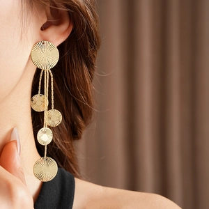 Detail of gold circular textured tassel earrings with layered chains on a model