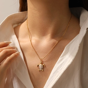 Close-up of a gold-plated turtle pendant necklace with white inlay on a female model