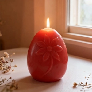 Red egg-shaped candle with floral embossing and lit flame on a white surface