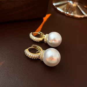 Macro detail of gold-plated hoop earrings with micro-pave zircons and white pearls