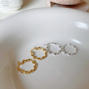 Detailed view of twisted wave hoop earrings in polished gold and silver finishes