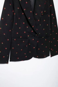 Détail de la broderie fraise et du bouton à boutonnage simple sur la veste noire
