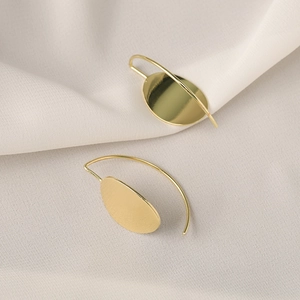 Detail view of golden geometric oval earrings on textured beige fabric background