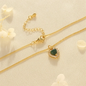 Macro shot of 18K gold plated heart necklace with green gem and zircon inlay