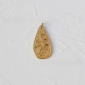 Detailed macro shot of a teardrop-shaped gold pendant with intricate floral engravings
