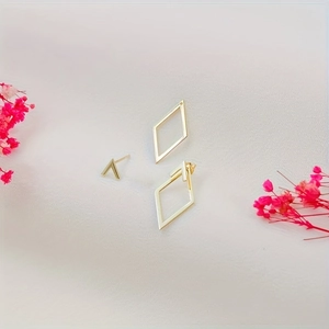 Parure de boucles d'oreilles losanges dorées et clou en V sur fond blanc avec fleurs