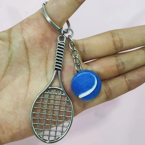 Detail view of tennis racket keychain with blue ball charm held in hand for scale