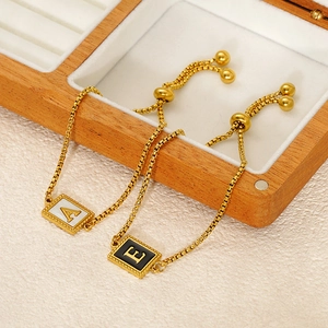 Macro shot of gold shell letter charms with adjustable box chain on a wooden box