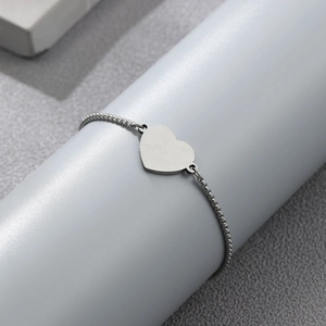 Minimalist stainless steel heart bracelet with bead chain displayed on gray pedestal