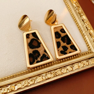 Vue détaillée de boucles d'oreilles dorées à motif léopard sur un fond cuir élégant