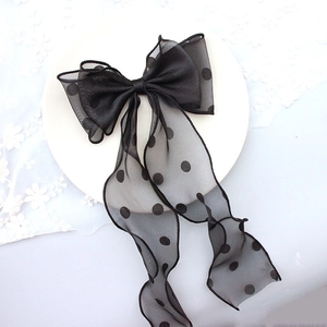 Detail view of a black polka dot tulle bow hair clip with ribbons on a white lace backdrop