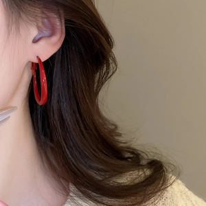 Detail of a large red C-shaped hoop earring with a glossy finish on a female model
