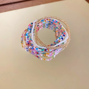 Close-up of bohemian multi-layer seed bead bracelet set with golden metallic accents on mirror