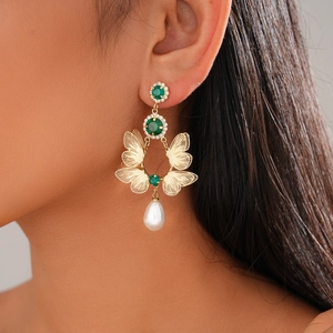 Close-up of double-layer butterfly earrings with green rhinestones and pearl drops on a model
