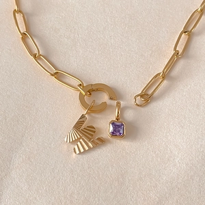 Primo piano di collana dorata con ciondolo a lettera M e gemma viola quadrata.