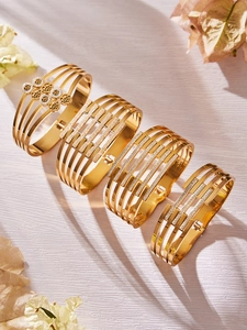 Dettaglio macro di bracciali dorati aperti con motivi floreali traforati e cristalli incastonati