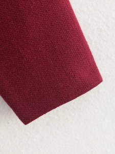 Makroaufnahme von dunkelrotem Strickstoff mit feiner Textur und Gewebe am Saum