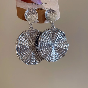 Macro shot of large silver geometric earrings with detailed circular ripple texture