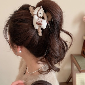 Detail view of a plush pony-shaped hair claw clip worn on a messy bun hairstyle