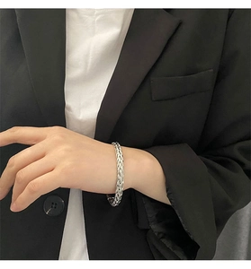 Detailed view of a silver woven chain bracelet worn on a female wrist over a suit