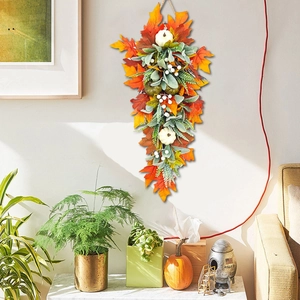 Fall teardrop wreath with white pumpkins and maple leaves hanging on a warm home wall