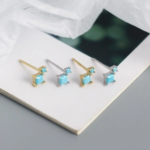 Macro shot of gold and silver geometric earrings with square turquoise zircons