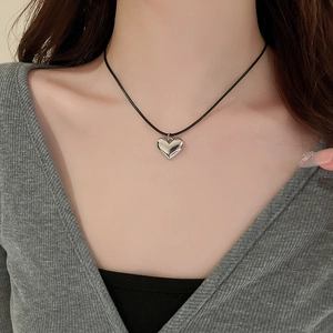 Close-up of a 3D silver heart pendant on a black cord necklace worn by a model