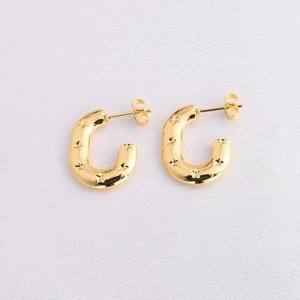 Macro view of C-shaped golden flower earrings with engraved star patterns on fabric
