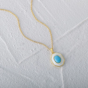 Detail of gold hummingbird necklace with turquoise stone and white inlay on stone background