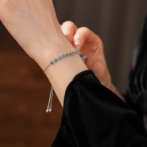 Detail of adjustable silver clover bracelet with green zircons worn on model's wrist