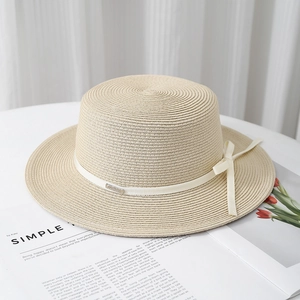 Detail of elegant boater hat with cream ribbon bow and metallic logo on white surface