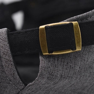 Detail of adjustable bronze metal buckle and black strap on gray cotton beret hat