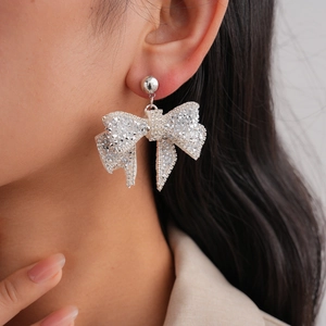 Close-up of elegant silver bow earrings with sparkling rhinestones worn on the ear