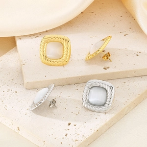 Detail view of square gold and silver cat-eye stone earrings on a natural stone base