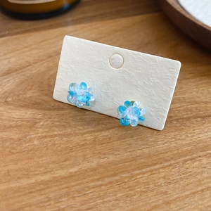 Macro detail of blue and white crystal flower stud earrings on a beige card